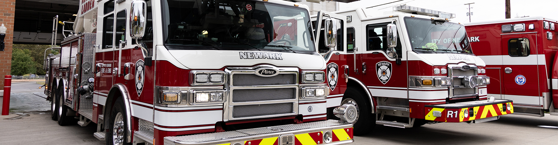 two red and white fire engines and one ambulance sitting outside of a fire station